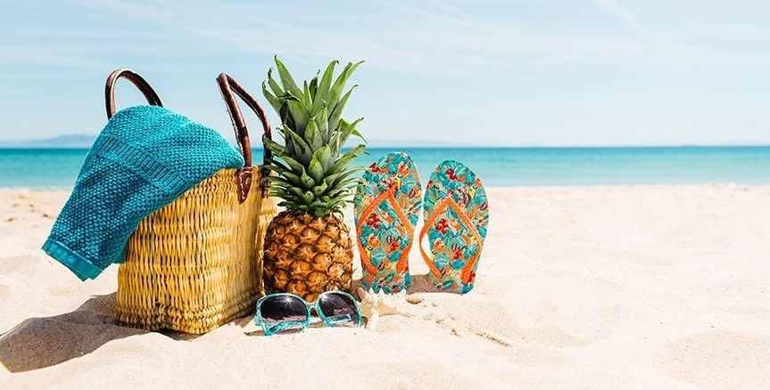 An image of the beach and on the sand there is a pair of female slippers, basket and a pineapple