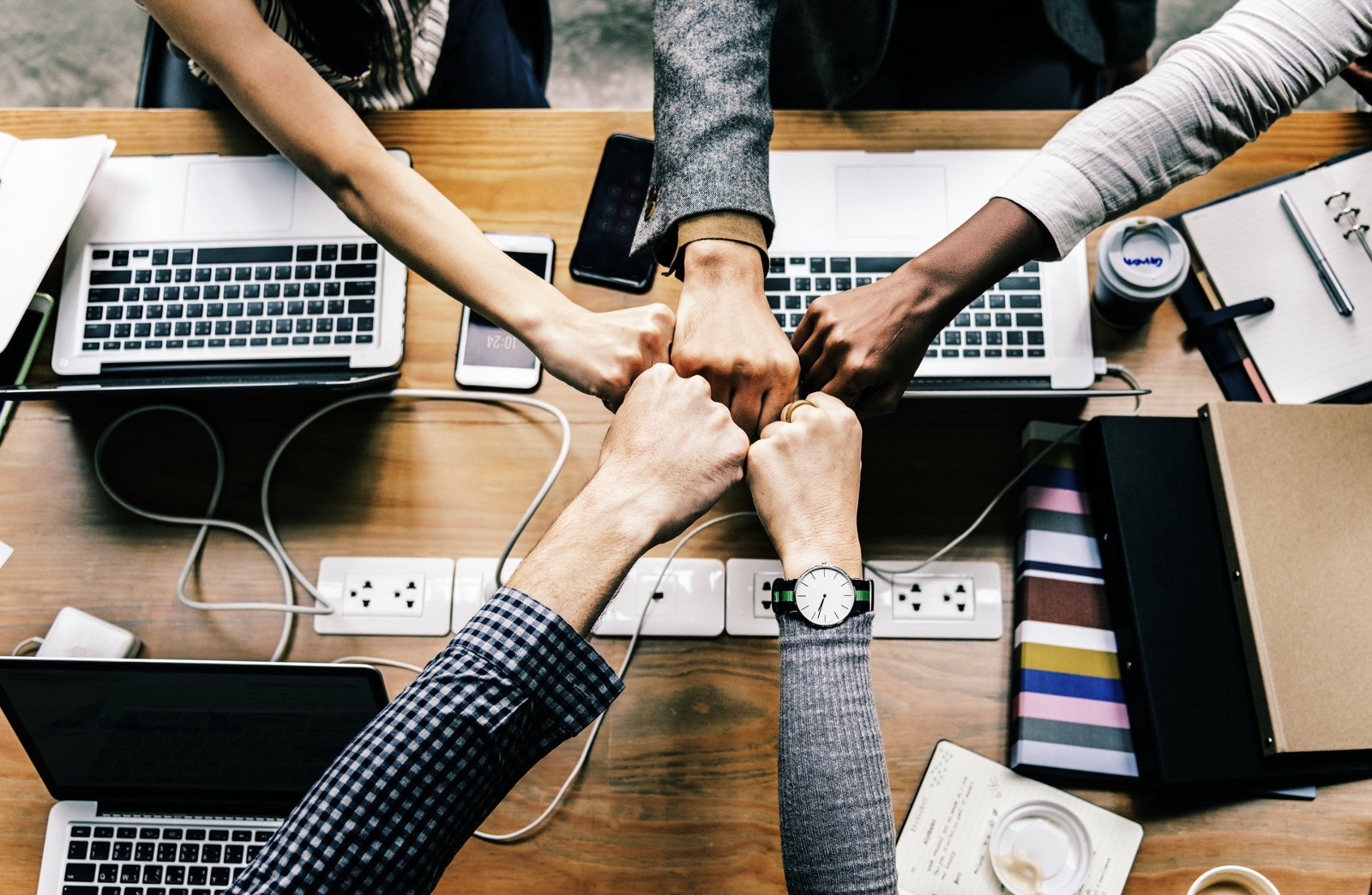 An image of five employees sitting at the same table each one with his own laptop and doing their hands like a fest to each other