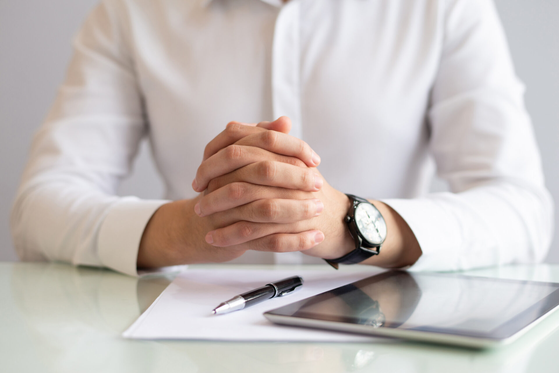 An image of an employee wearing a white formal shirt and brown watch holding his hands together