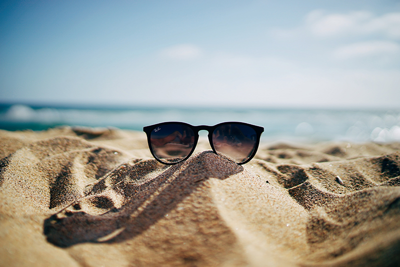 An image of the beach with pair of sunglasses on the sand