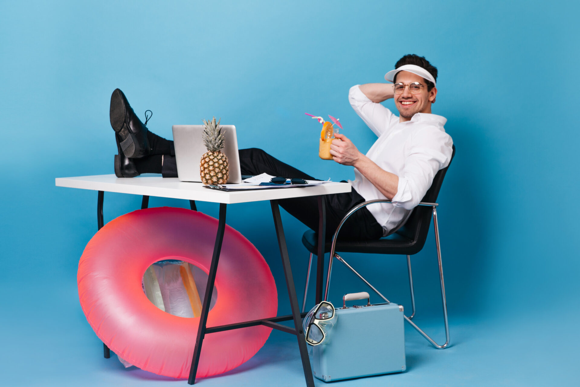 cap-works-vacation-drinks-cocktail-guy-is-sitting-table-with-suitcase-inflatable-circle-laptop-pineapple-scaled