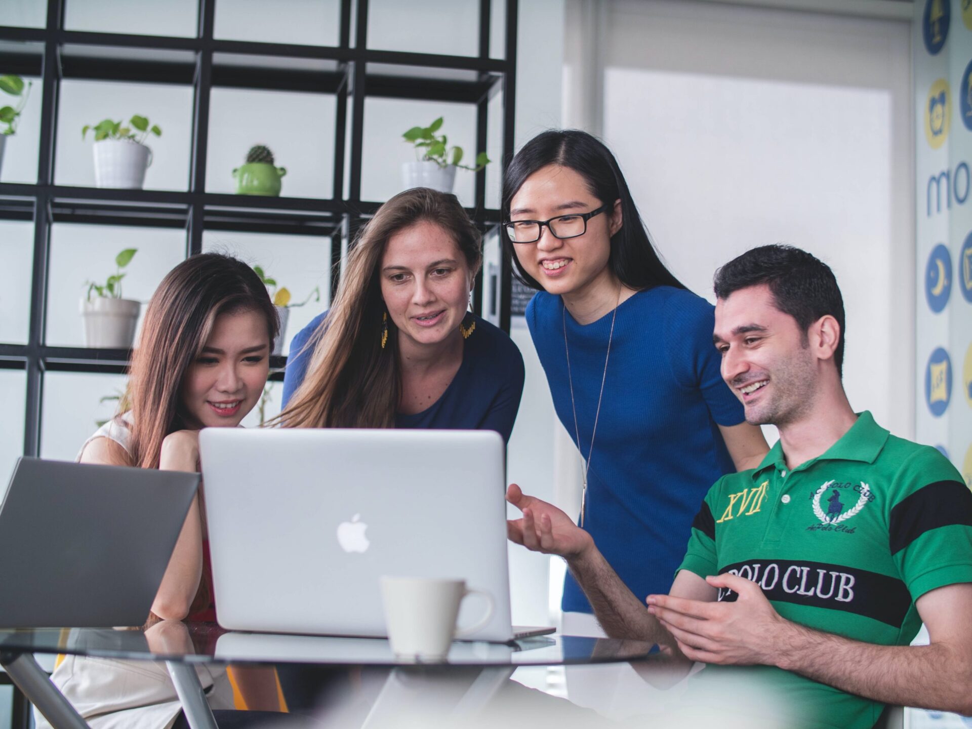 An image of 4 employees looking at the same laptop as if they are attending the same video call.
