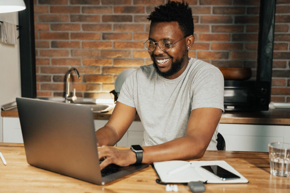 A male employee is seated at his desk, typing on his laptop with a smile on his face, appearing engaged and happy with his work.