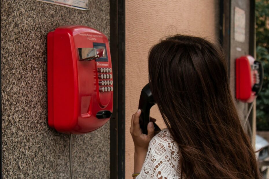 An image of a female employee talking on a public telephone hanged on the wall in the middle of the street.