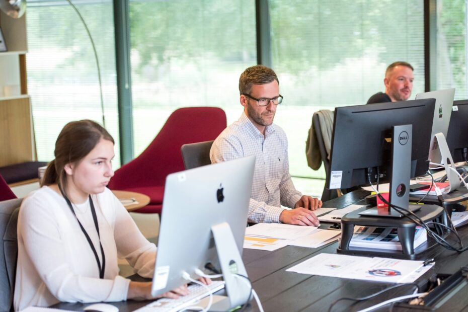 An iamage of three employees in the same office each one is sitting in front of his laptop