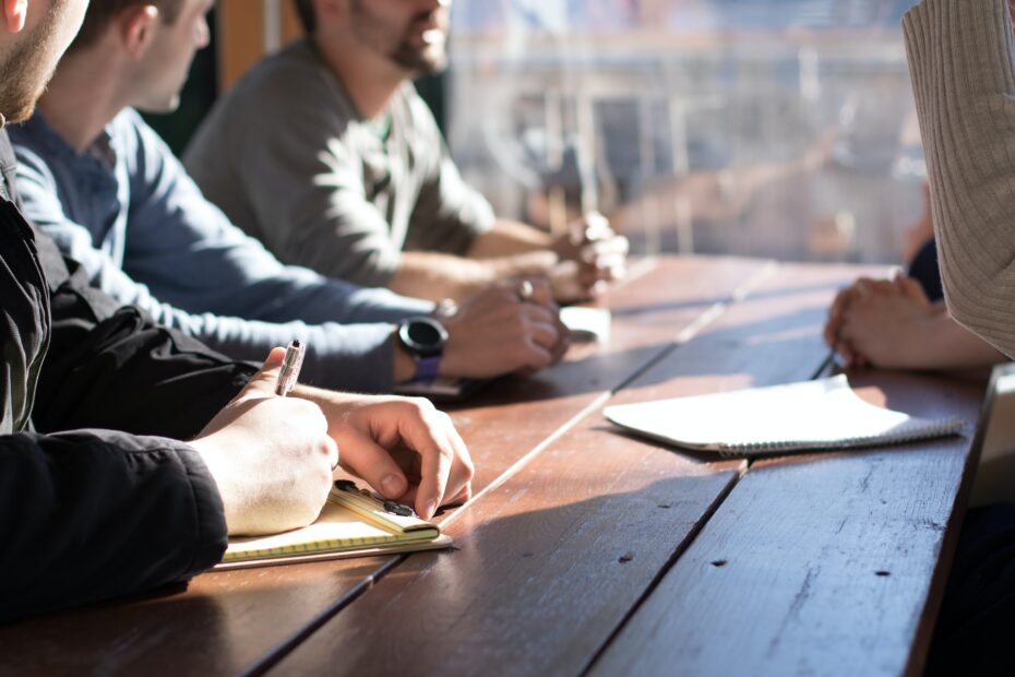 A close up of employees sitting on a wooden table taking notes.