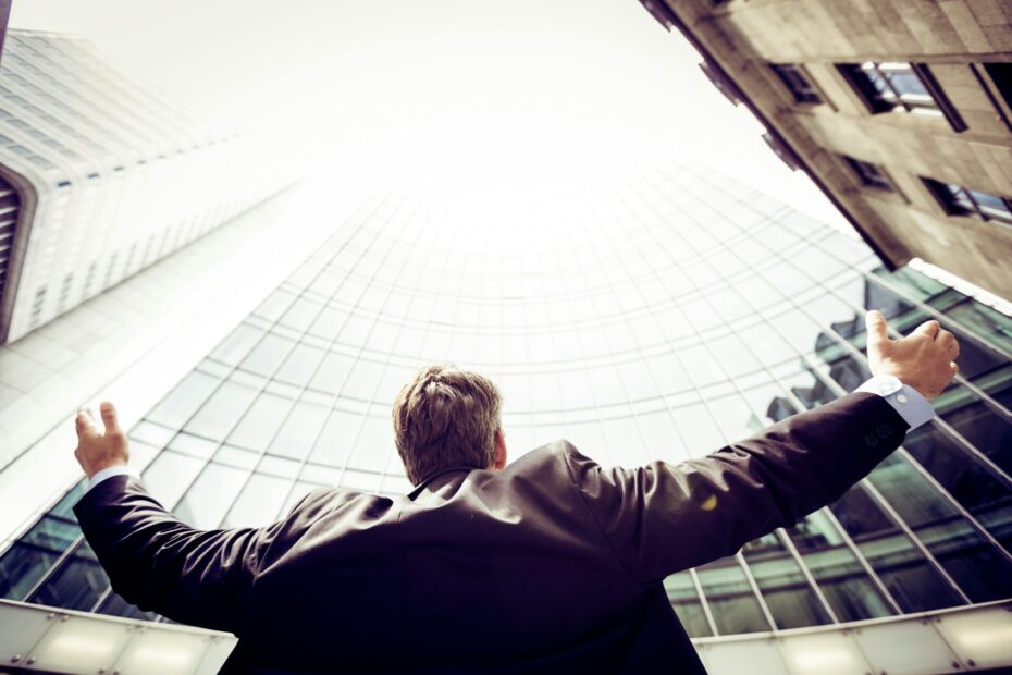 An image of an employee standing Infront of his company building while opening his two hands