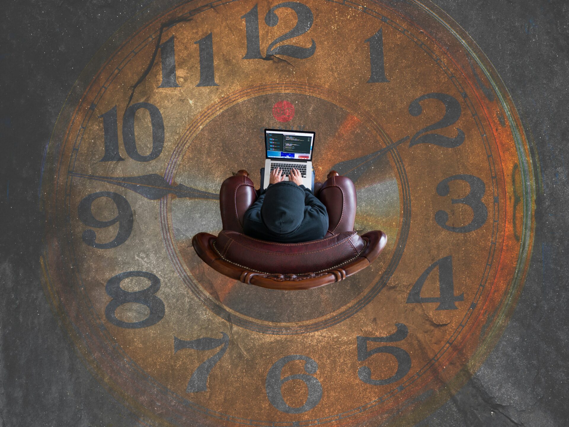 An image of an employee sitting at a desk, deeply focused on working on a laptop, with a large clock prominently displayed in the background, symbolizing time management