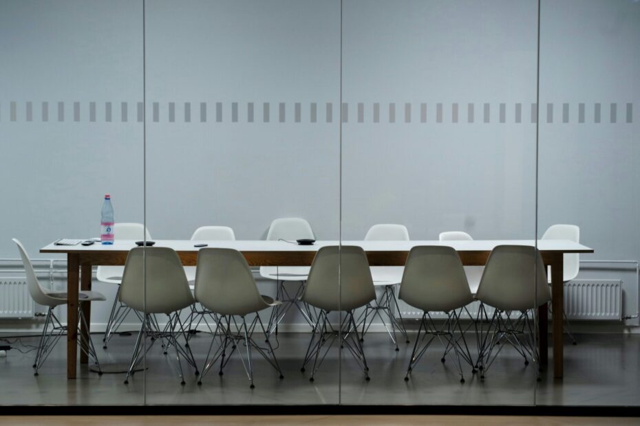 A picture of an empty meeting table in a conference room, set up with chairs around it, ready for a meeting. The setting is professional and neat.