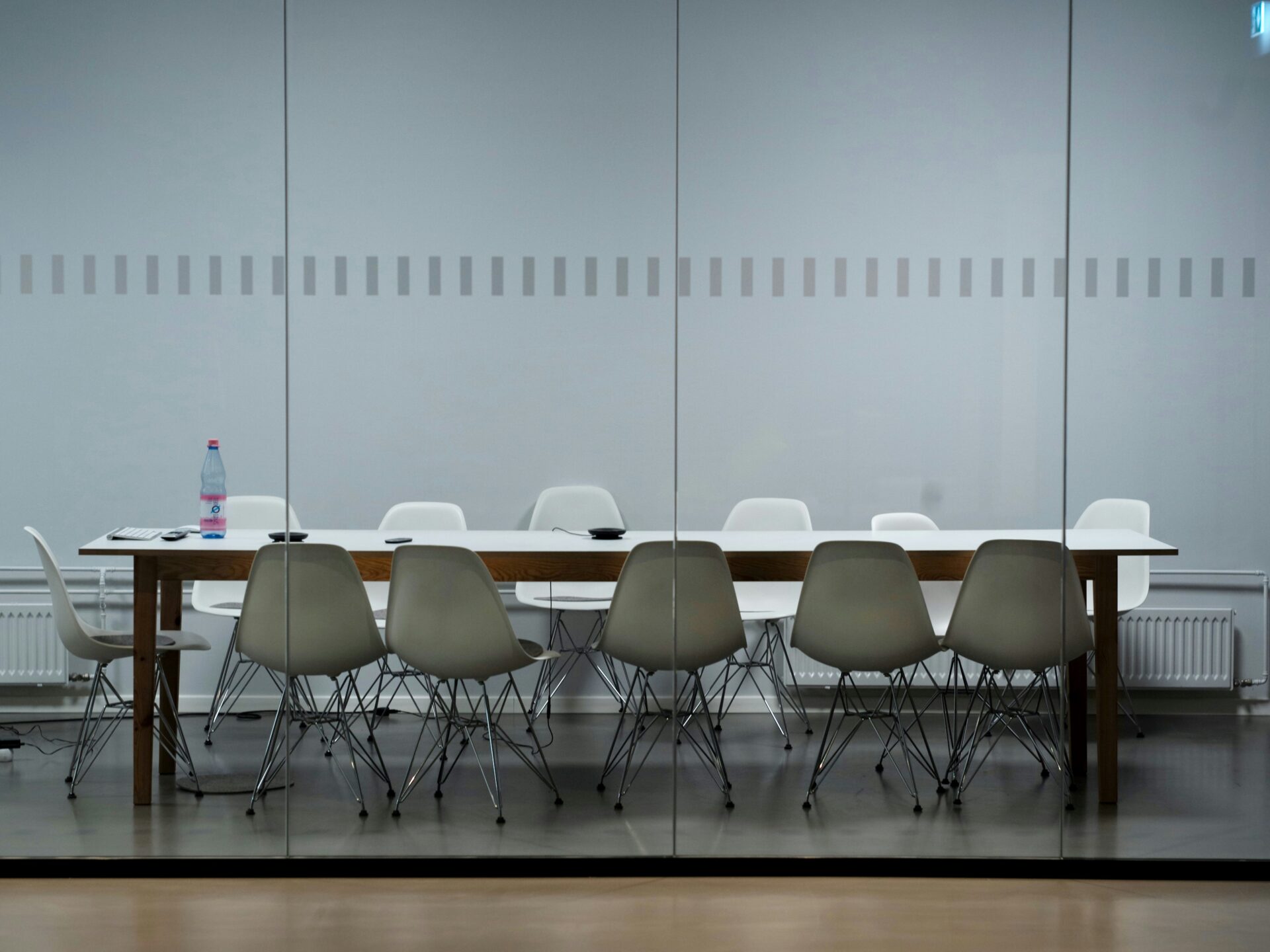 A picture of an empty meeting table in a conference room, set up with chairs around it, ready for a meeting. The setting is professional and neat.
