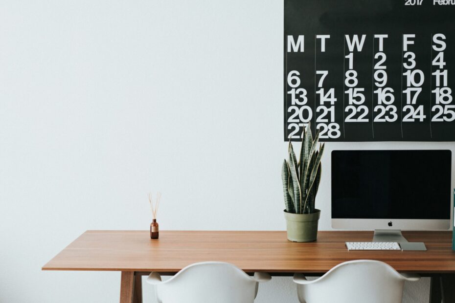 Laptop on a wooden desk and a calendar hanged on the wall.