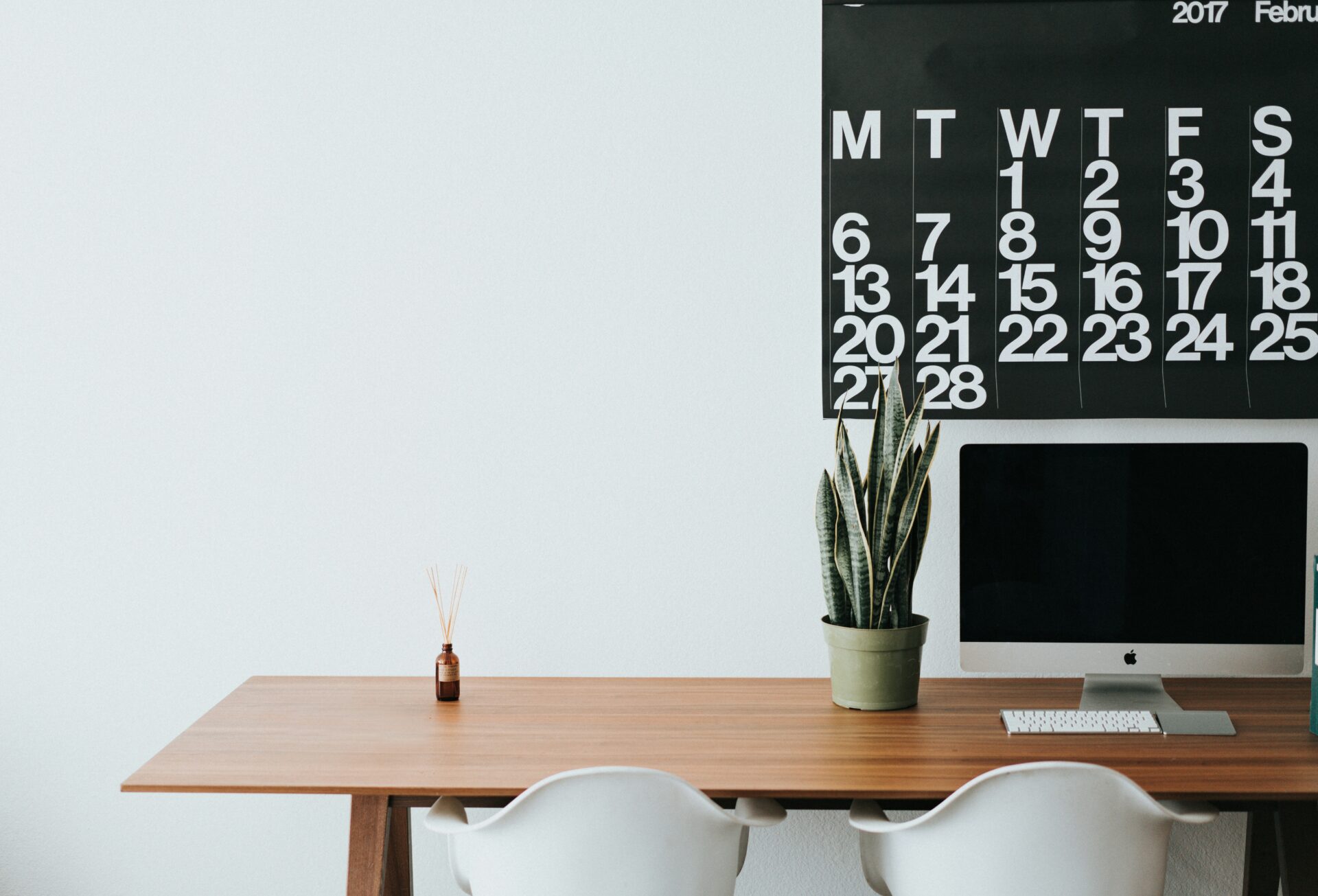 Laptop on a wooden desk and a calendar hanged on the wall.