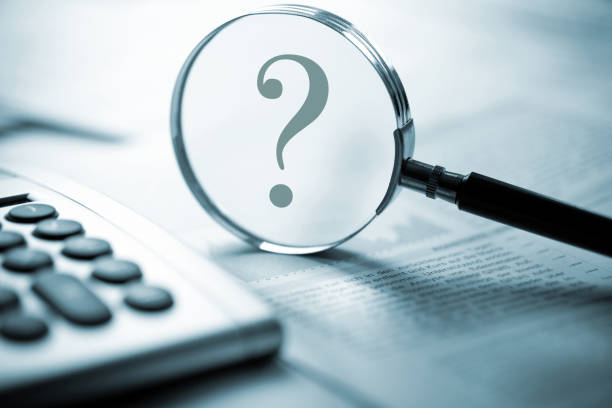 question mark in magnifying glass on desk above stock market new. Buy, sell, hold?