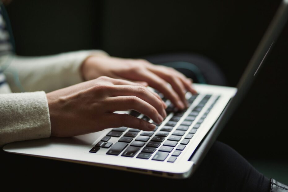 An image of a laptop placed on a person's lap, with two hands typing on the keyboard.