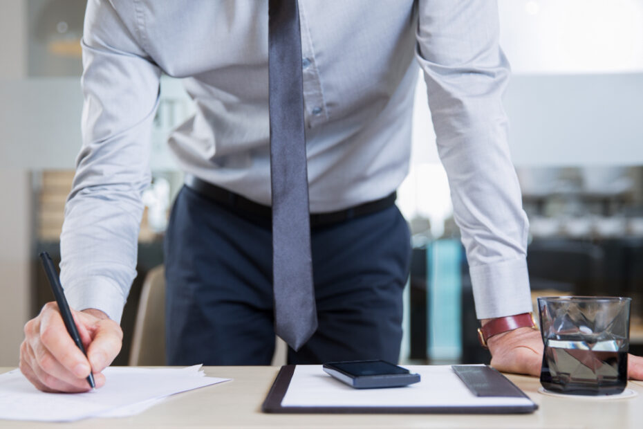 A man standing Infront of his disk signing a contract.