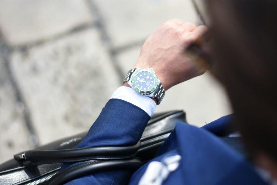 a man wearing blue suit, and a professional silver watch, holding a black leather bag.