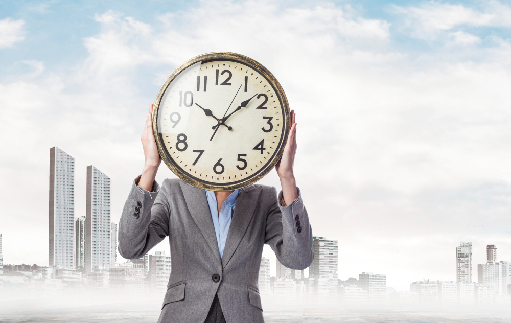 A person in a business suit stands against a cityscape background, holding a large clock in front of their face, symbolizing the concept of time management and the importance of tracking time effectively.