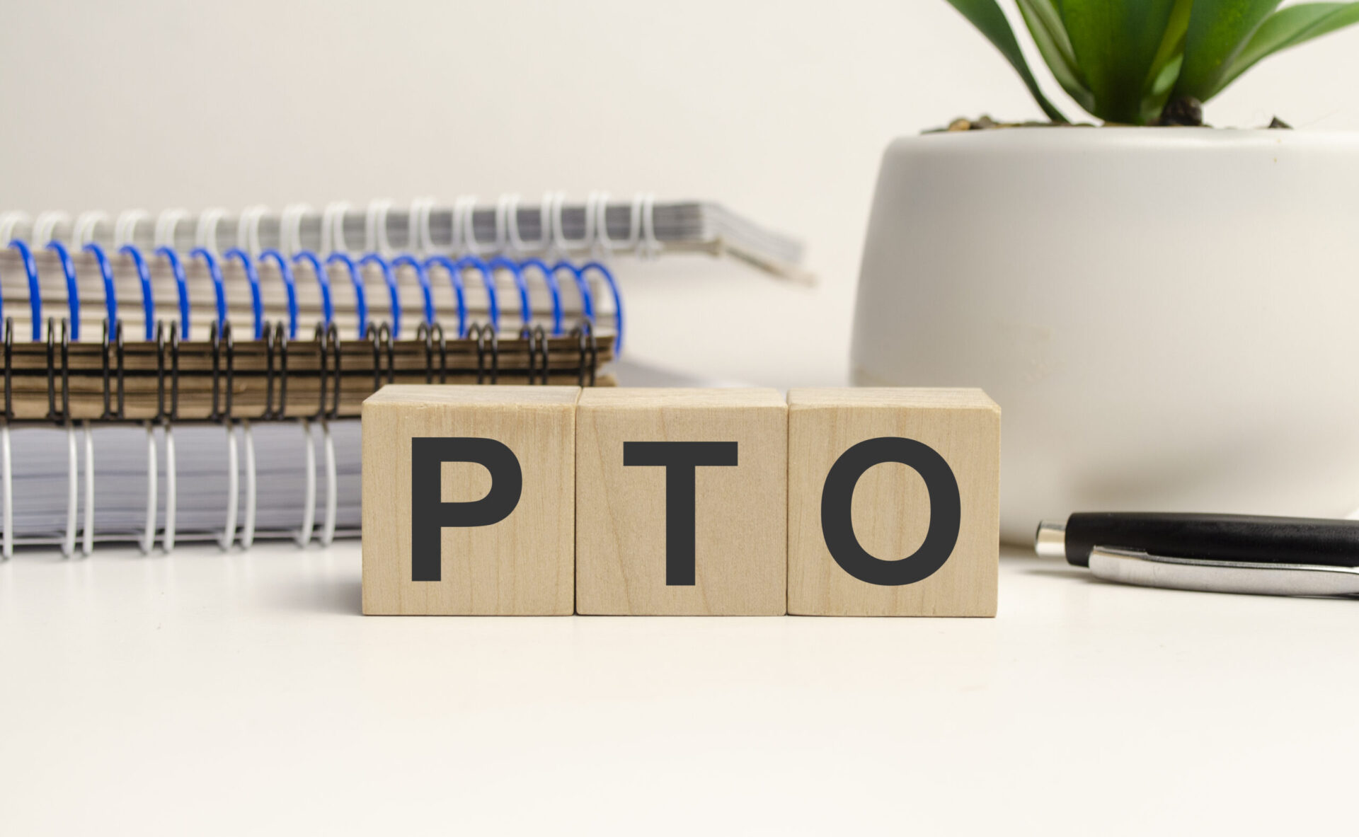 Wooden blocks spelling 'PTO' placed on a desk with office supplies, symbolizing PTO payout policies and workplace benefits.