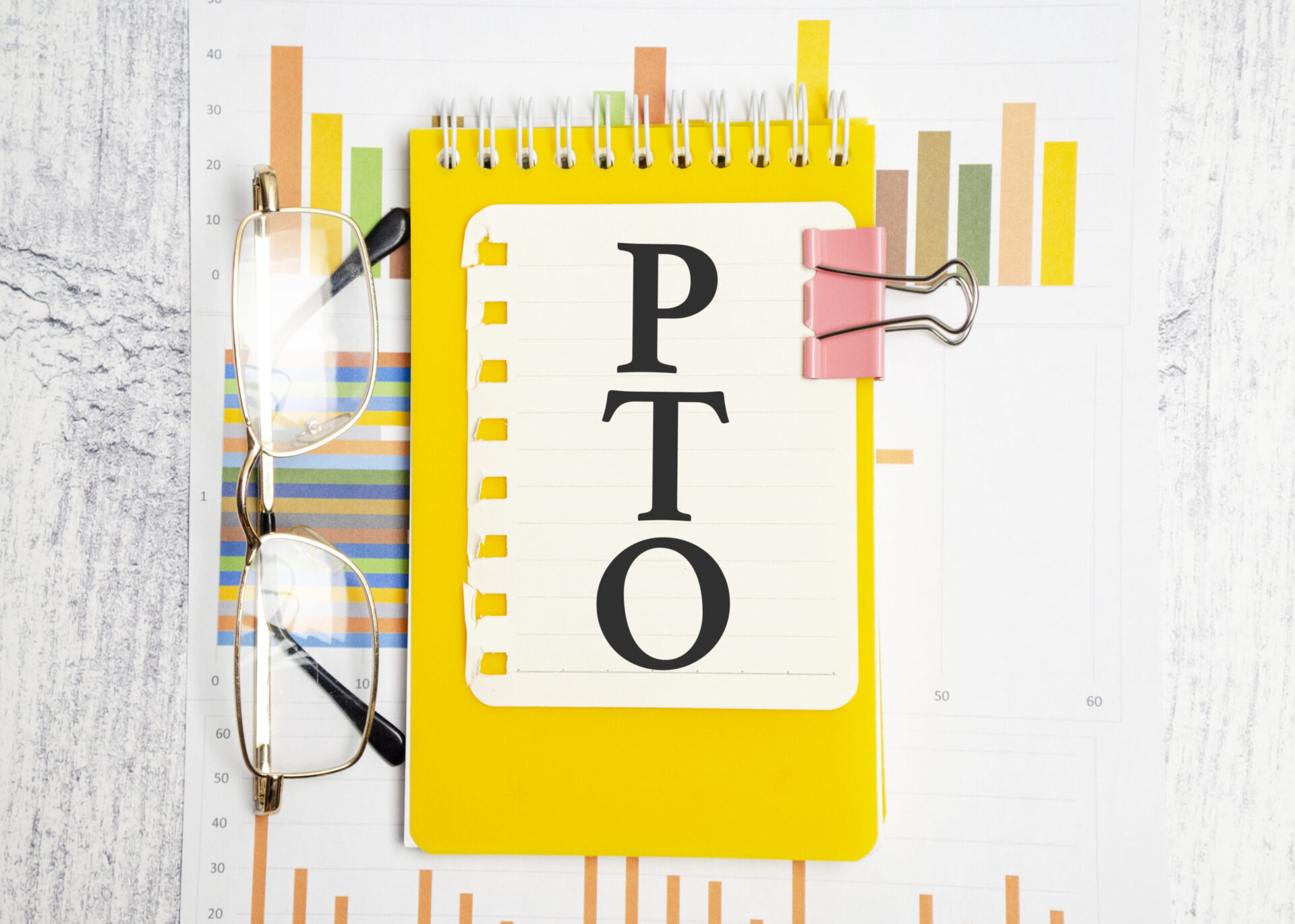 Yellow notebook with 'PTO' written on the cover, placed on a background of colorful charts and graphs, representing the concept of a vacation accrual calculator for tracking paid time off.