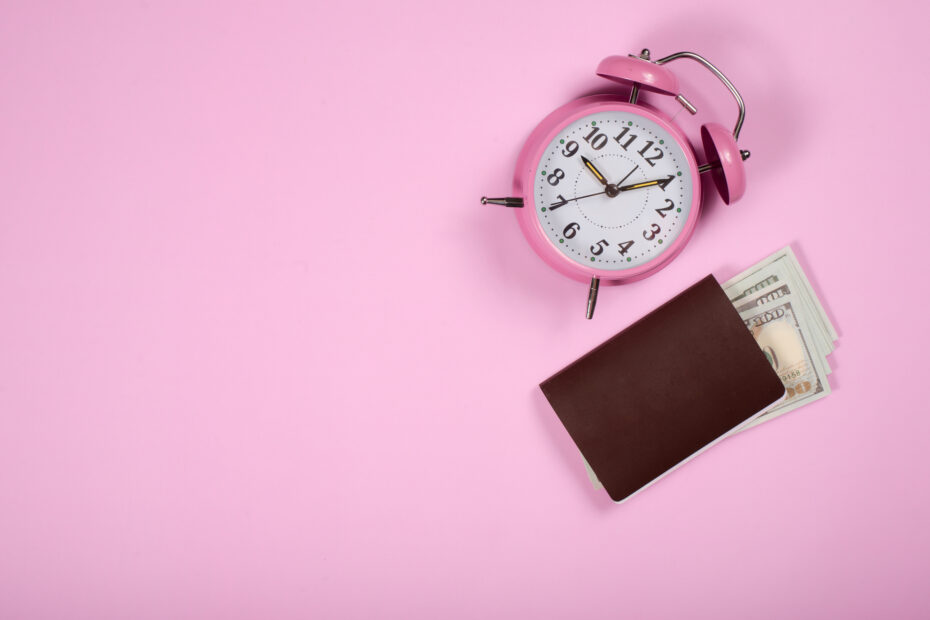 Pink alarm clock and a brown wallet with cash on a pastel pink background, symbolizing Paid Time Off (PTO) and financial security.