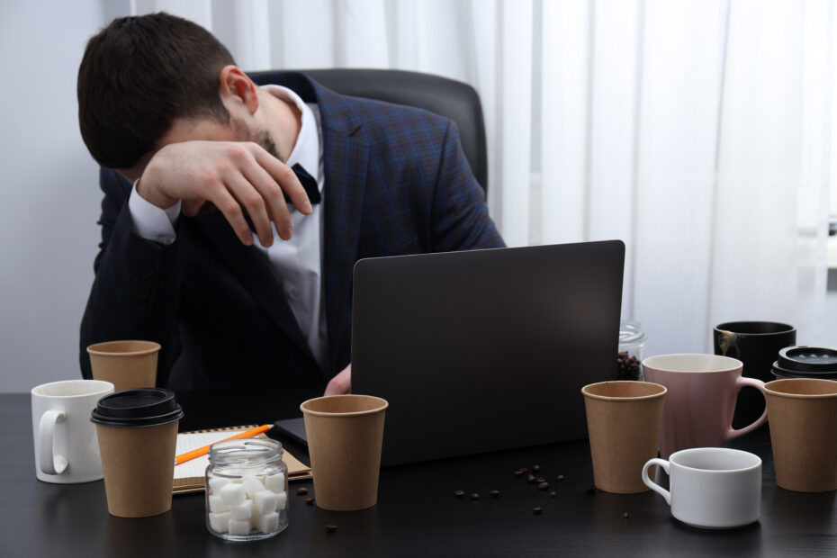 Exhausted employee working through unpaid break surrounded by coffee cups, illustrating the toll of being overworked and denied rest during designated break times.