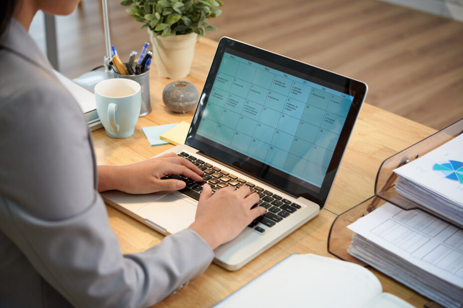Employee using timesheet software on a laptop to manage work schedule and calendar tasks in an office setting